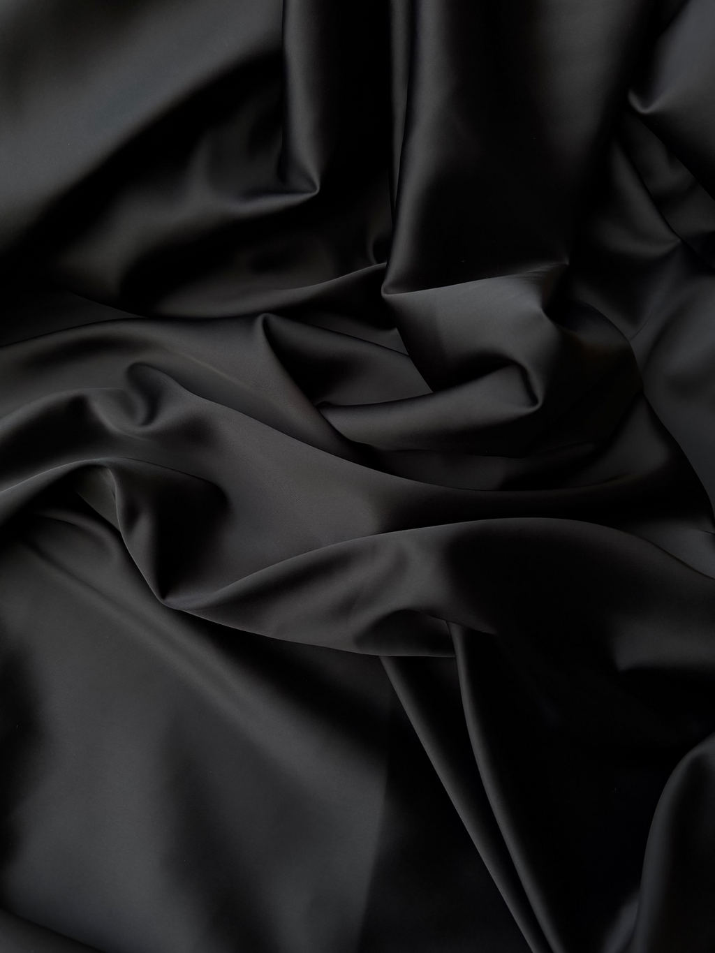 Dettaglio tessuto doppio raso fluido nero intenso, superficie liscia e lucente per abbigliamento
