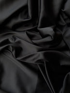 Dettaglio tessuto doppio raso fluido nero intenso, superficie liscia e lucente per abbigliamento
