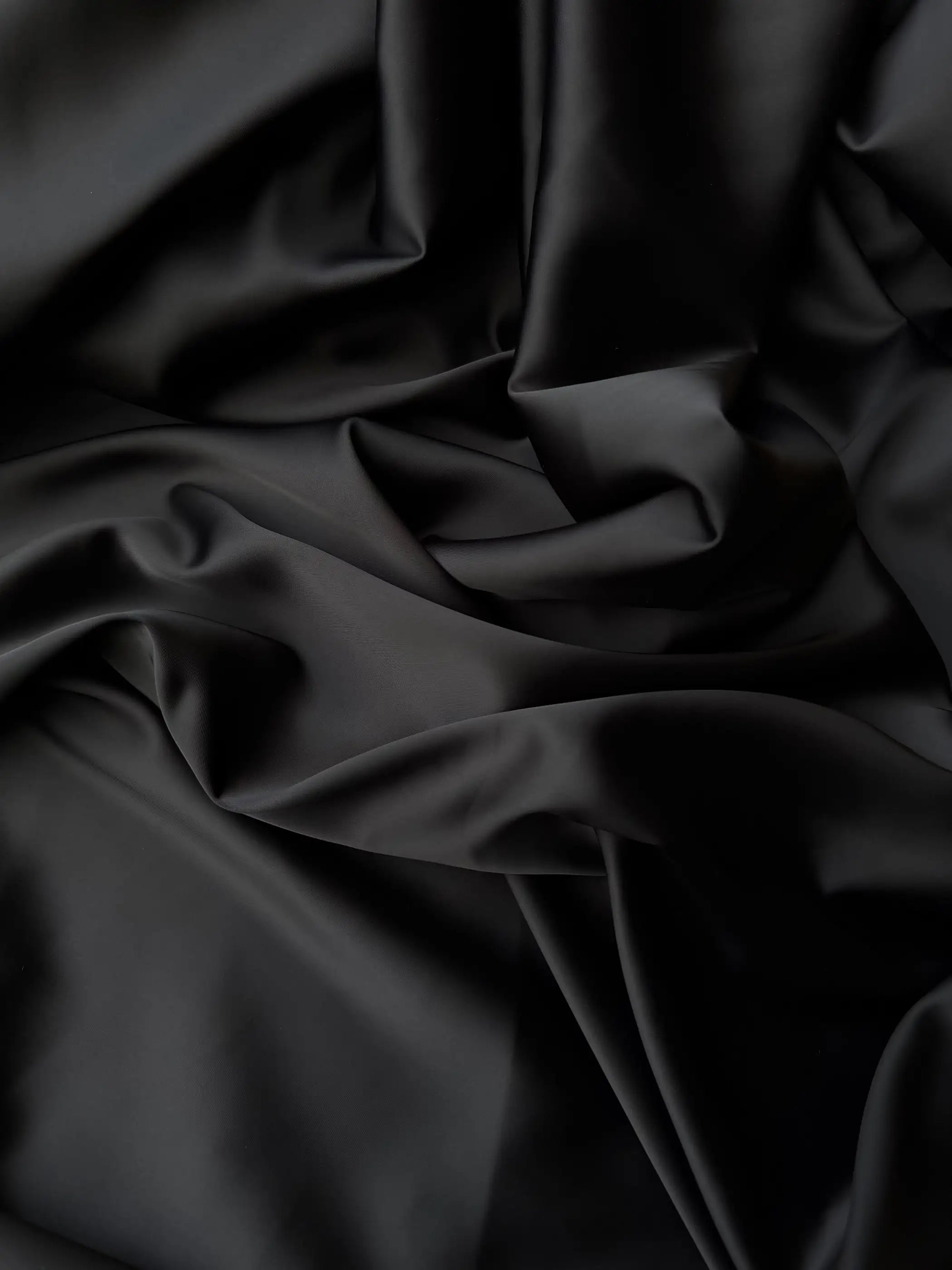 Dettaglio tessuto doppio raso fluido nero intenso, superficie liscia e lucente per abbigliamento
